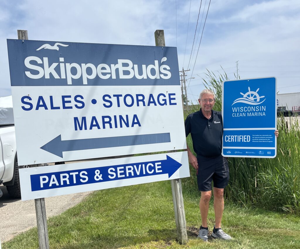 Man standing next to skipper bud's sign holding their new clean marina sign.