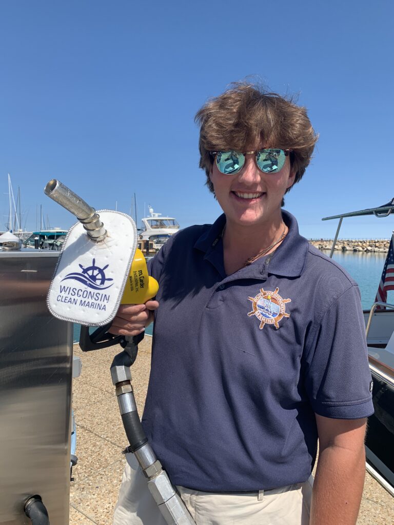A person holding a gasoline pump with a Wisconsin Clean Marina sign.